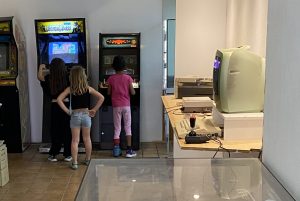 Drei Kinder stehen vor zwei der Sielautomaten im Computeum. Im Vordergrund dieht man Homecomputer die auch zum Spielen einladen.