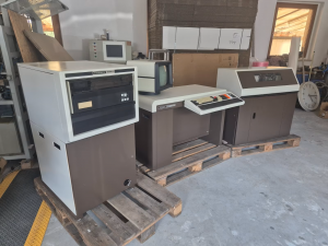 TA 1100, eingabaut in einem Tisch mit eingebauter Tastatur und aufgesetztem Monitor, links daneben ein turmartiger Schrank mit der Fest/Wechselplatte, links daneben der Drucker. Alles auf Paletten.