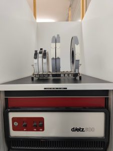 In einer Nische steht ein Dietz 621 Minicomputer. Oben auf steht ein Gestell, ähnlich wie zum trocknen von Tellern, in dem 10 Halterungen für Bänder sind. In sechs davon stehen Bänder. 3 Kleine und 3 Große.