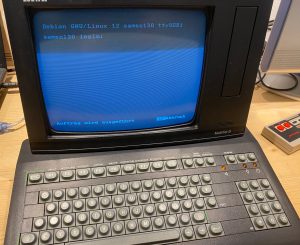 Das MultiTel-D vereint in einem schwarzen Pultgehäuse eine Tastatur mit Alphateil, Funktionstasten und Nummernfeld mit einem kleinen schwarz/weiß Bildschirm. oben auf ist ein Telephonhörer. Der Bildschirm zeigt die Ausgabe eines Linux-Systems